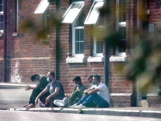 A group of men, thought to be migrants, sit outside in the sunshine after arriving yesterday night at Napier Barracks in Folkestone, Kent. Credit;PA