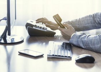 Businessman use the phone in the office, keyboard, mouse, mobile, and monitor detail in the background