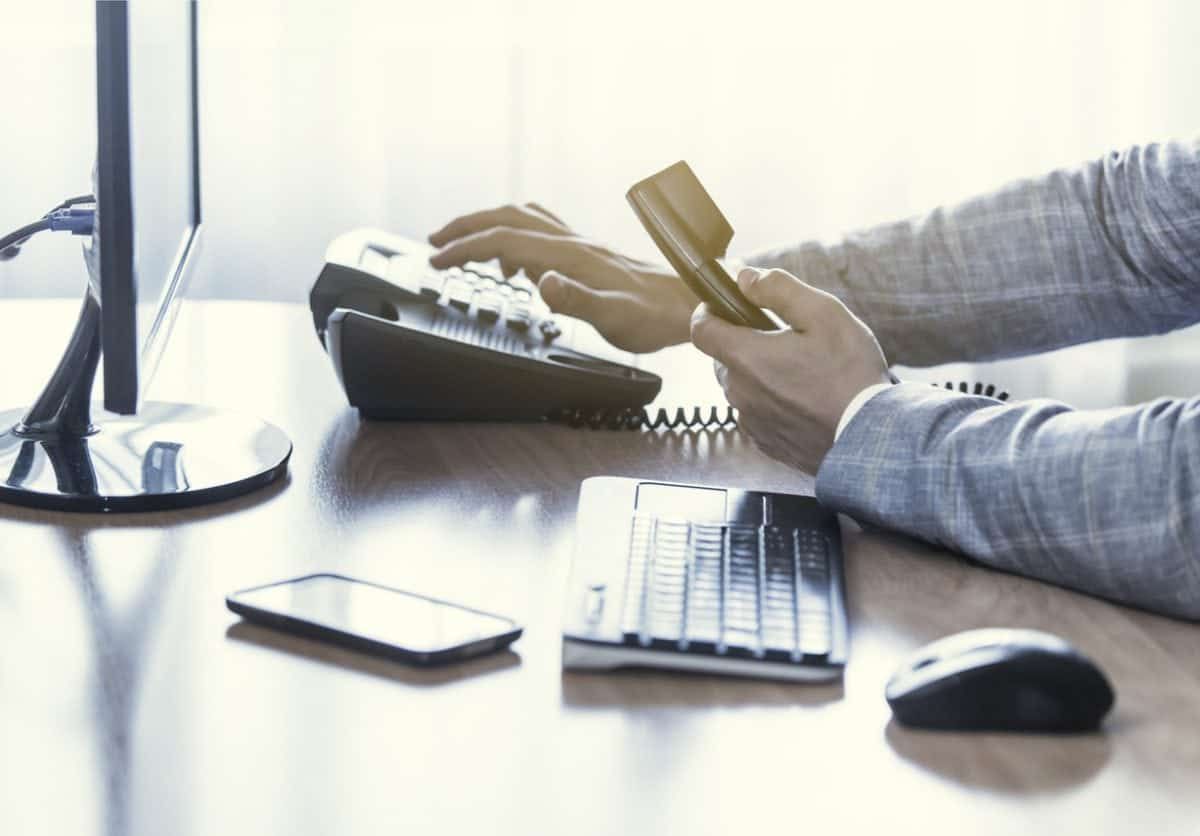 Businessman use the phone in the office, keyboard, mouse, mobile, and monitor detail in the background