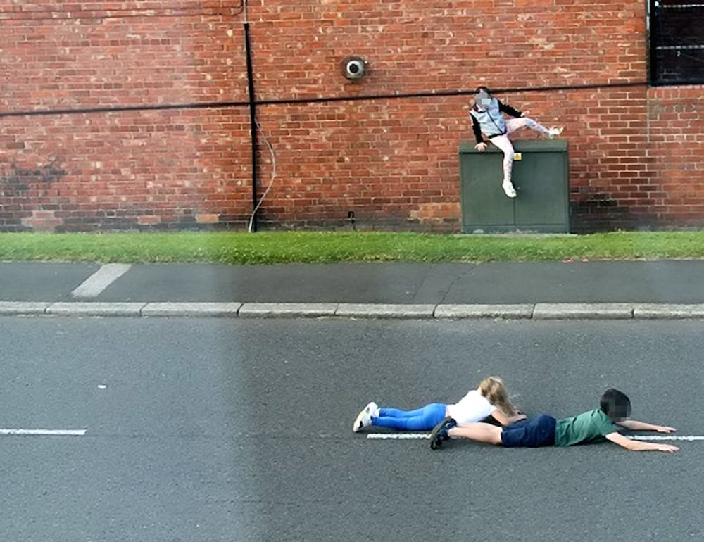 These shocking photographs show children dicing with death as they dodge cars by lying in the middle of a busy ROAD. See ROSS PARRY story RPYCHICKEN.  The three children appear to be playing 'chicken', a game involving waiting as long as possible in the way of cars, before jumping away at the last second.  In one of the images, two of the children are seen lying in the middle of the road, while another image shows one the children running out on to the road as a car speeds past.  The photographs, which were taken in Washington, Tyne and Wear, were sent to police by local councillor Dianne Snowdon after local residents raised concerns.  Officers from Northumbria Police are working to identify the children in the images so their parents can be spoken to about their reckless behaviour but police also want to remind people of the dangers of playing on and near busy roads.