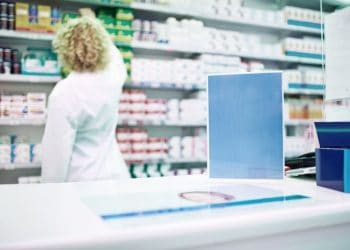 Shot of a blank board on the counter of a pharmacy with a pharmacist working in the background