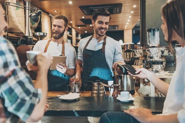 Smiling barista with barcore reader accepting smart phone payment