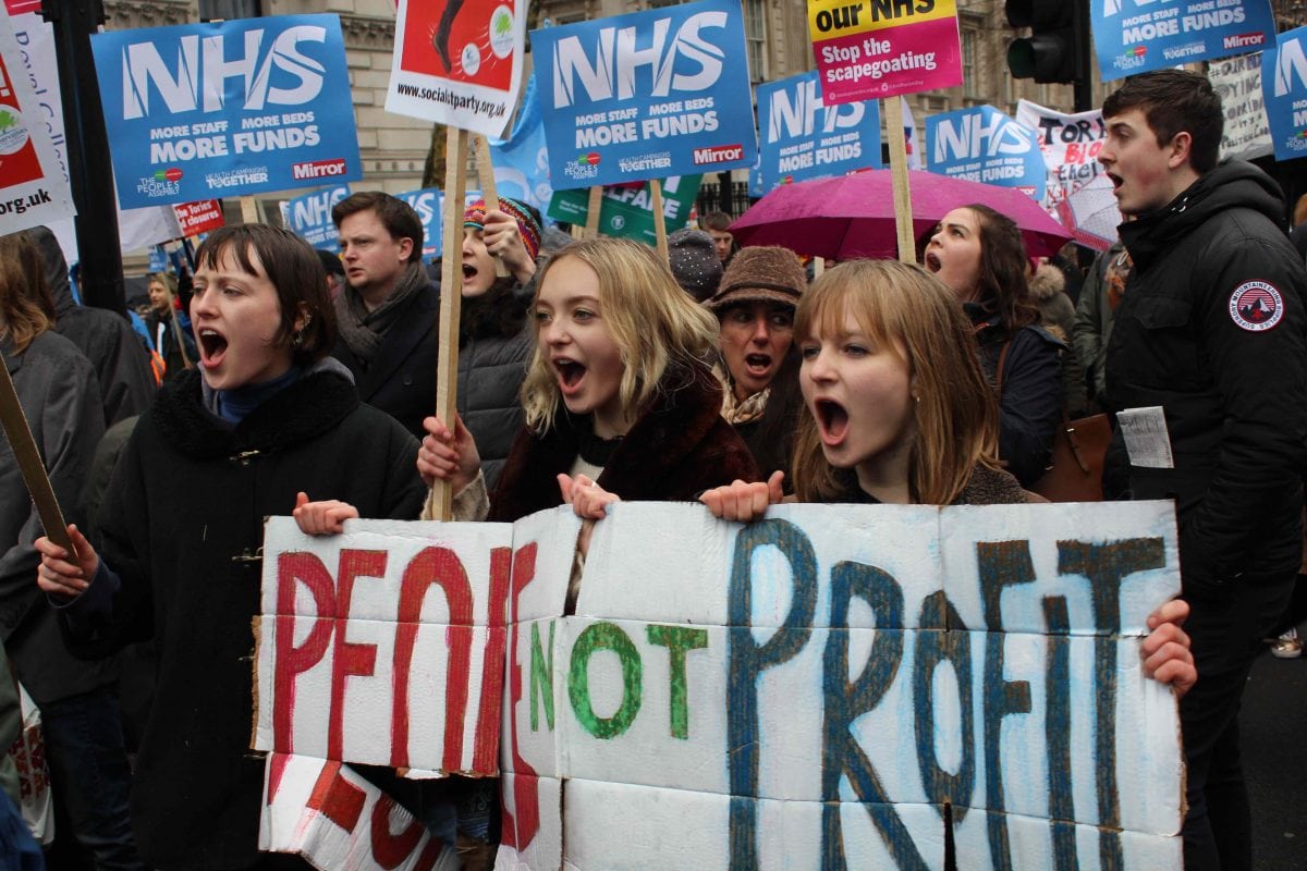 Three young activists hold a 'people not profit sign'