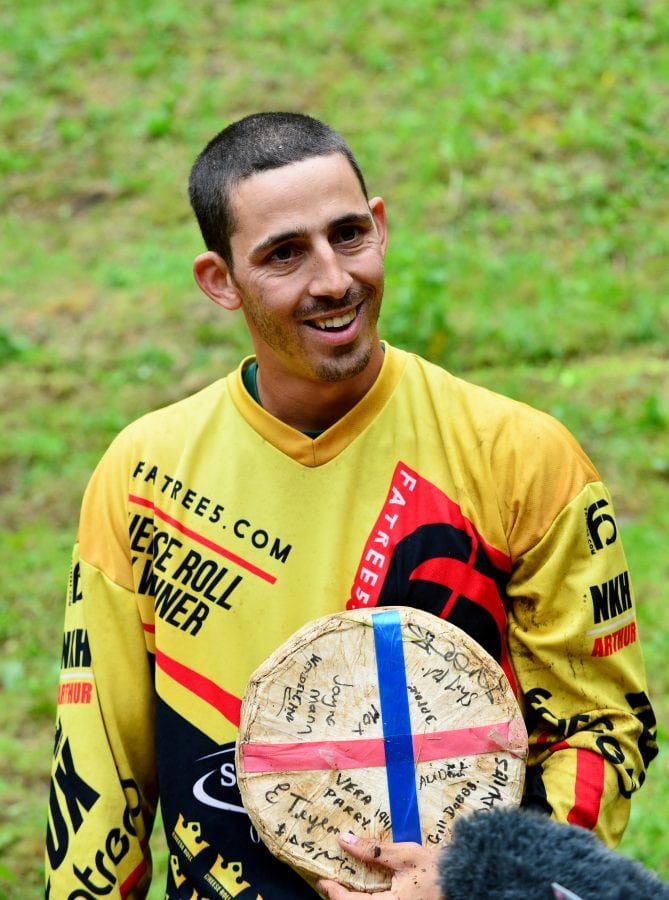 A soldier was named the gratest athlete in the world today after his record-breaking 21st win - at CHEESE-ROLLING. Legendary cheese-chaser Chris Anderson risked life and limb - well mainly limb - hurling himself into the record books for chasing a wheel of Double Gloucester down a super-steep hill.