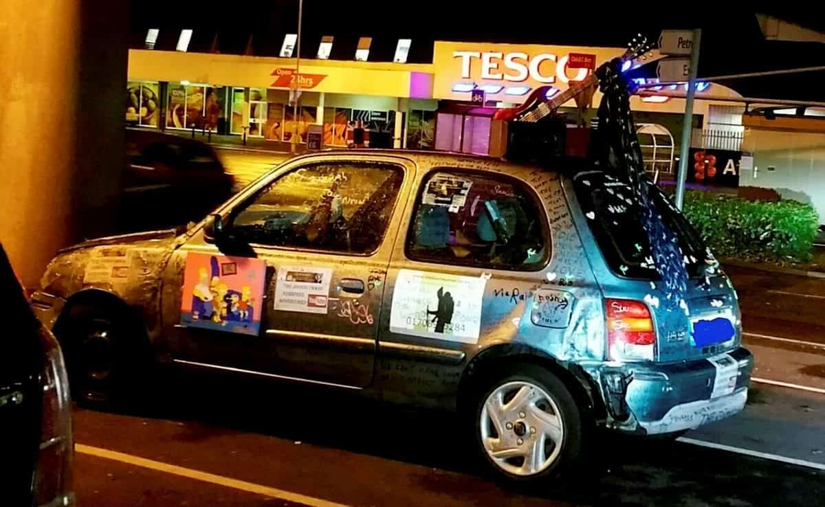 Car with Simpsons portrait on door and guitar on roof taken off road by police
