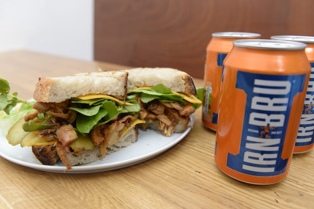 Cafe owner Amelia Sulhunt, from Serenity Now Cafe, Glasgow, Scotland, with a Vegan Irn Bru sandwich made from pulled Jackfruit. The Jackfruit is roasted after Irn Bru is poured on it.   See SWNS story SWSCsandwich; A family-run vegan cafe is set to make taste buds across the city explode with the launch of a new Irn Bru infused winter sandwich. Serenity Now Cafe will soon offer the juicy sandwich served on toasted sourdough bread with BBQ sauce, rocket, cheese and pickles. And the Irn Bru is roasted with pulled jackfruit and mushrooms in the barbecue sauce. The mouthful bite also comes with side-salad, air-fried chips or mac and cheese. Glaswegians have been flocking to try the £6.50 sandwich which will be sold at the cafe based at Great Western Rd, Glasgow.