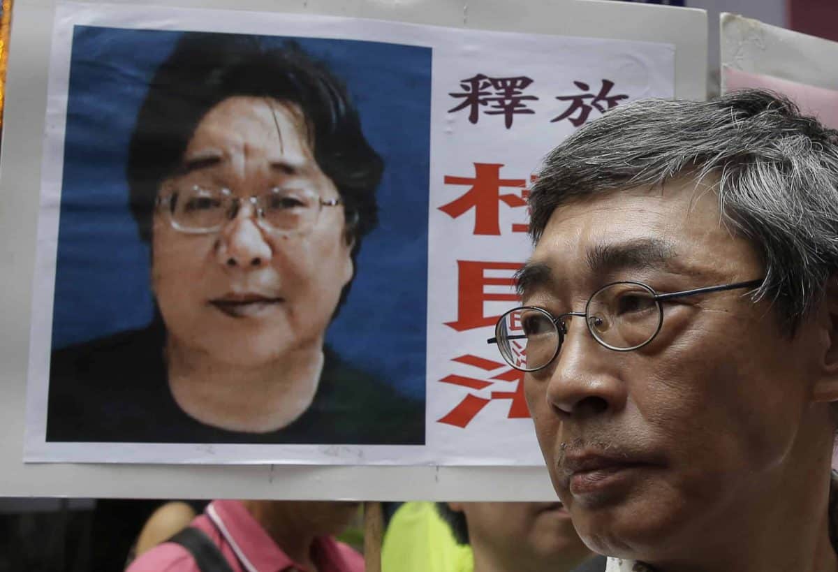 A picture of missing bookseller Gui Minhai is shown on a placard beside freed Hong Kong bookseller Lam Wing-kee, as the protesters are marching to the Chinese central government's liaison office in Hong Kong. A court in eastern China announced Tuesday, Feb. 25, 2020, that it has sentenced Gui, a naturalized Swedish citizen, to 10 years in prison. (AP Photo/Kin Cheung, File)