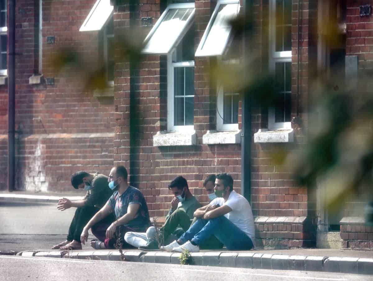 A group of men, thought to be migrants, sit outside in the sunshine after arriving yesterday night at Napier Barracks in Folkestone, Kent. Credit;PA