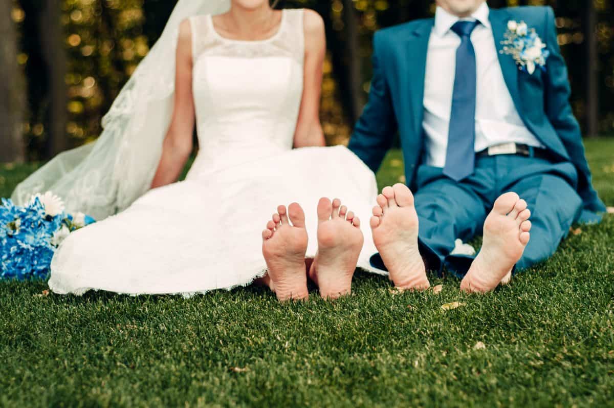 barefooted young fair-haired bride and her fiance sits on the grass in an exotic park, in a long white dress with a bouquet of flowers in her hands, a walk after the wedding ceremony, a wedding ceremony