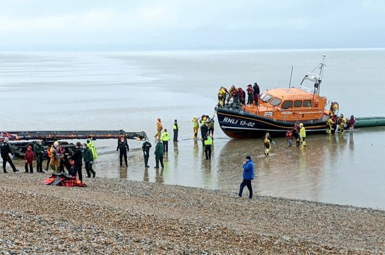 A lifeboat crew assist migrants from the English Channel in Dungeness, Kent.  November 20, 2021.  See SWNS story SWOCmigrants.  Hundreds of migrants were rescued from the sea by RNLI lifeguards after crossing the Channel in small boats.  Adults and young children wrapped in blankets were seen being led up the beach in Dungeness, Kent on Saturday (20/11).  They were helped by lifeguards from RNLI Dungeness after attempting to seek asylum before the winter weather makes the journey too difficult.  At least four dinghies packed with dozens of people reportedly reached the shore, as well as a lifeboat bringing in more from out at sea.  Others arrived at Folkestone and Dover harbours, brought in by authorities.  Border Force agents and police were on the scene as well as three coaches to pick the migrants up and take them to be processed.