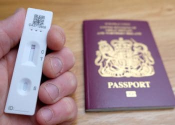 File photo dated 07/05/21 of a person holding a negative lateral flow Covid-19 test in front of a passport for the United Kingdom of Great Britain and Northern Ireland. New rules will come into force from October 24, in time for families returning from half-term breaks, allowing travellers arriving in England to take cheaper lateral flow tests rather than PCR test. Travellers who take a test at home must take a photo of their test and booking reference, and send this to the private test provider to verify the results. Transport Secretary Grant Shapps has said the change in policy for the post-arrival test is "based on trust". Issue date: Friday October 15, 2021.