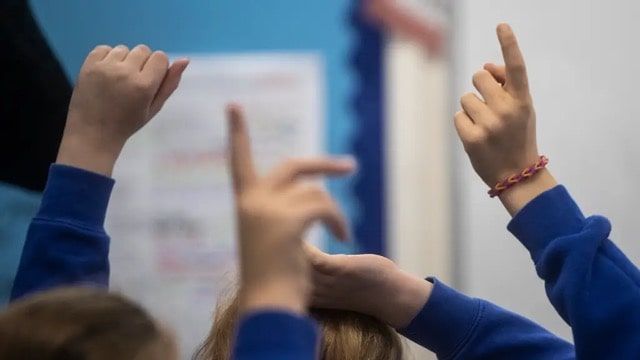 Children raising their hands in a classroom.
